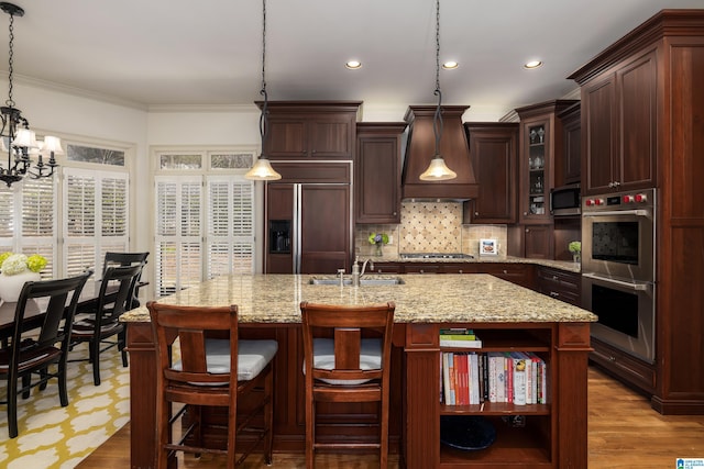 kitchen featuring premium range hood, appliances with stainless steel finishes, tasteful backsplash, a center island with sink, and crown molding