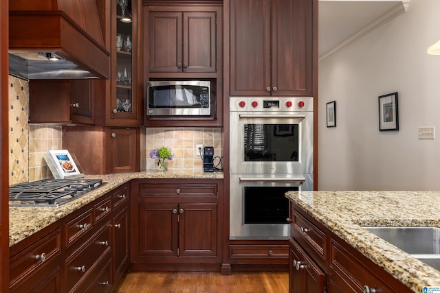 kitchen featuring light stone counters, stainless steel appliances, tasteful backsplash, dark wood finished floors, and glass insert cabinets