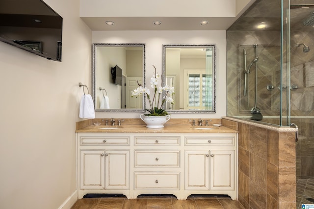 full bath featuring double vanity, tiled shower, a sink, and recessed lighting