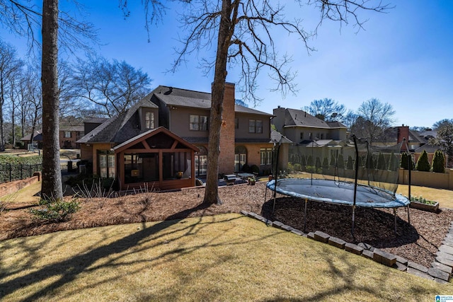 rear view of property with a yard, a trampoline, a chimney, and a sunroom