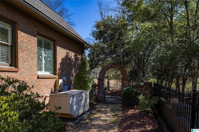 view of side of property featuring central AC unit, a gate, fence, and brick siding