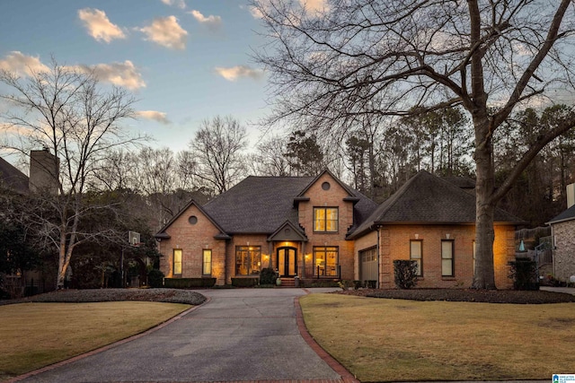 view of front of house with roof with shingles, aphalt driveway, a lawn, and brick siding