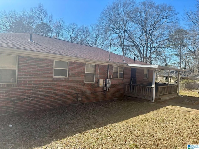 view of property exterior featuring brick siding, roof with shingles, and a wooden deck