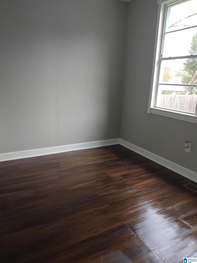 unfurnished room with dark wood finished floors, visible vents, and baseboards