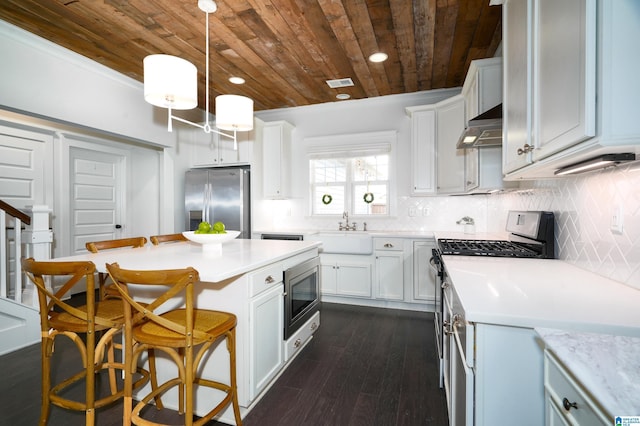 kitchen featuring light countertops, decorative backsplash, appliances with stainless steel finishes, under cabinet range hood, and a kitchen breakfast bar