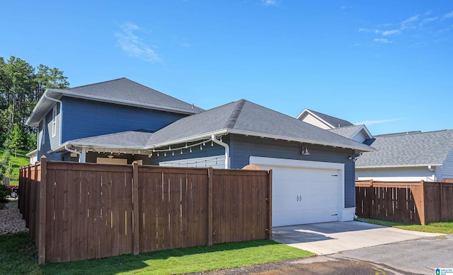 view of property exterior featuring a garage, concrete driveway, fence, and a shingled roof