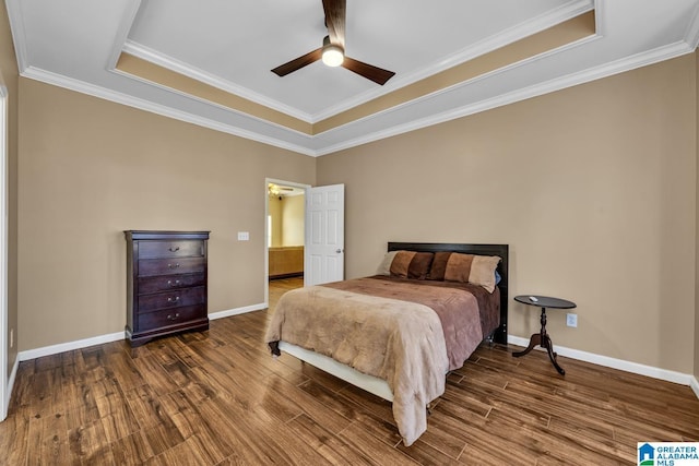 bedroom with crown molding, a tray ceiling, wood finished floors, and baseboards