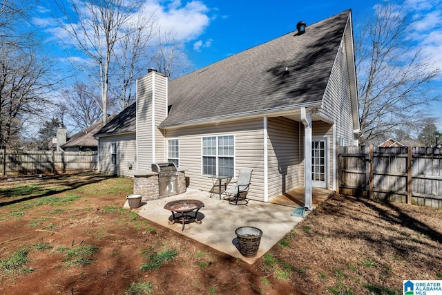 rear view of house with a shingled roof, a fire pit, a patio, a fenced backyard, and a chimney