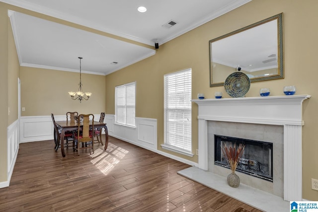 dining area featuring a wainscoted wall, visible vents, a premium fireplace, ornamental molding, and wood finished floors