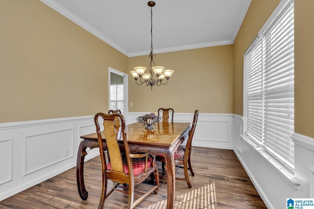 dining space with dark wood-style floors, crown molding, a notable chandelier, and a wainscoted wall