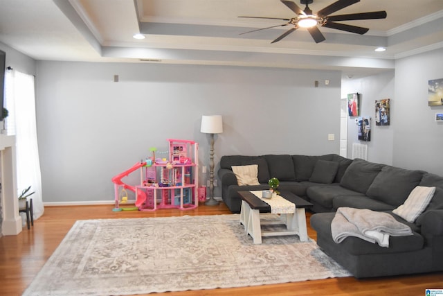 living room with crown molding, a ceiling fan, a raised ceiling, and wood finished floors