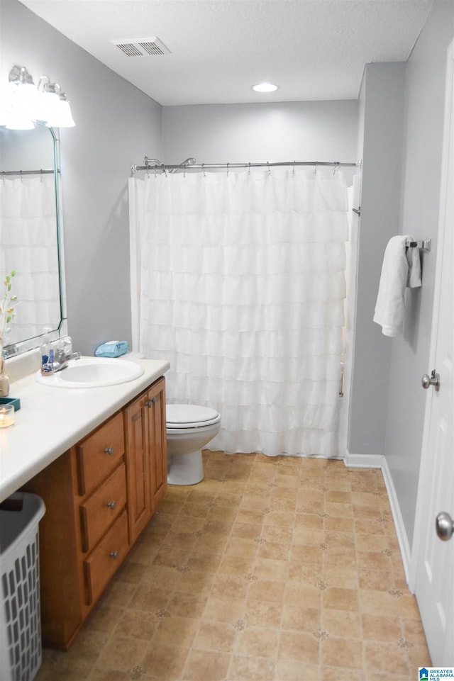 full bath featuring visible vents, toilet, vanity, a textured ceiling, and baseboards