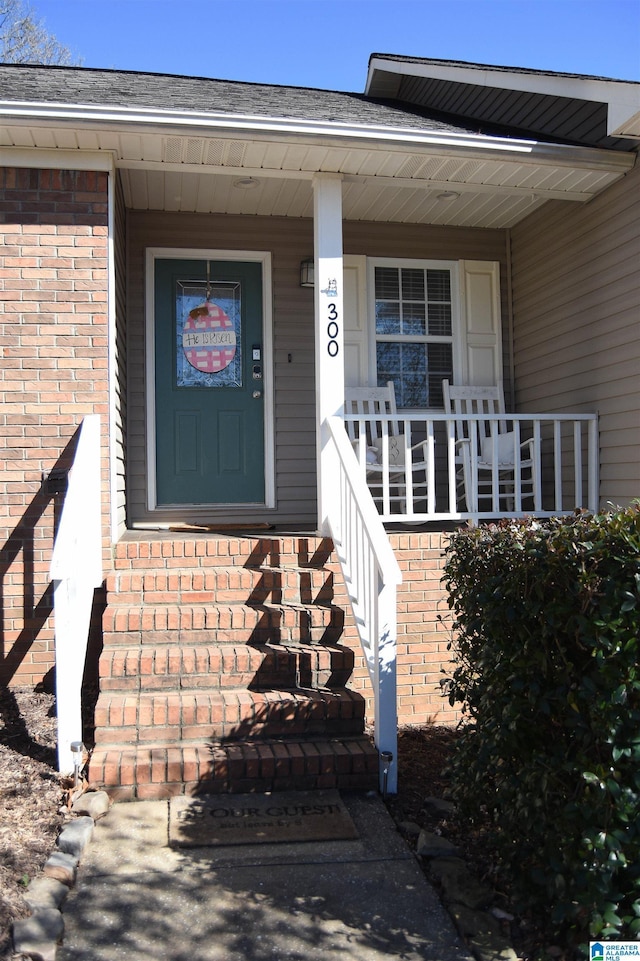 property entrance featuring a porch and brick siding