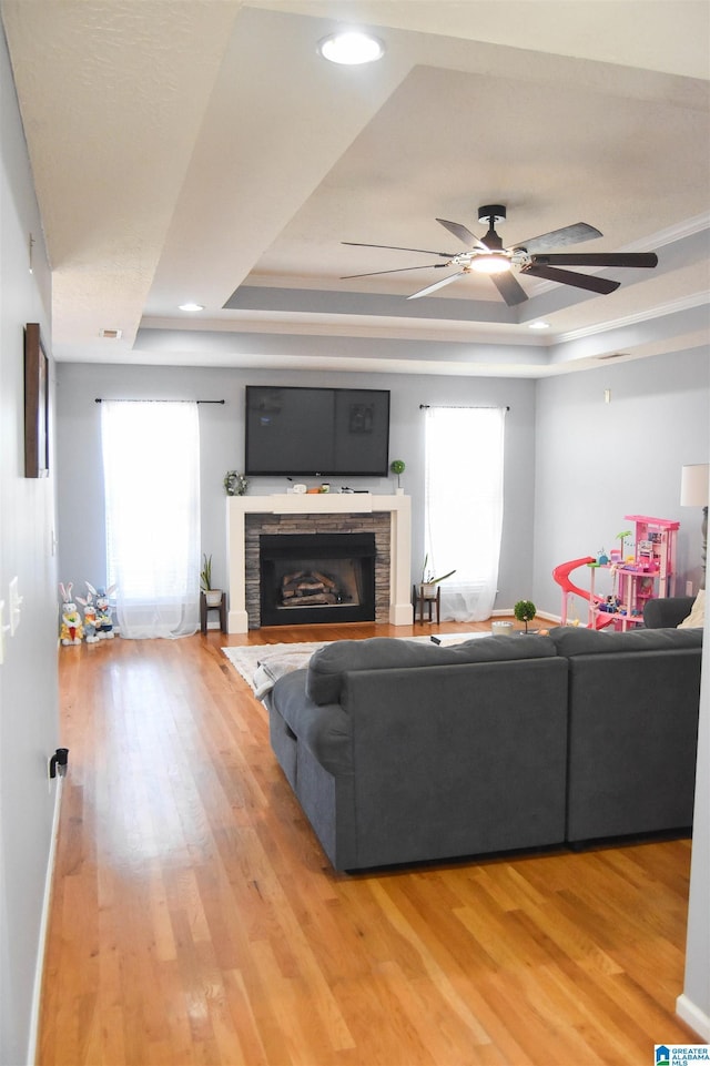 living area featuring a tray ceiling, a fireplace, light wood finished floors, and ceiling fan