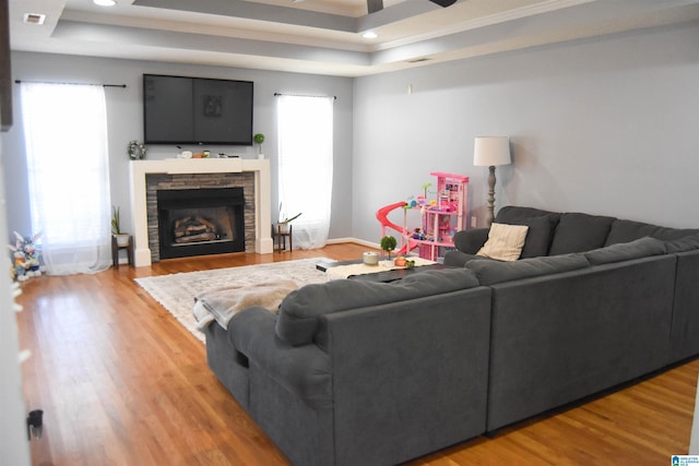 living room with visible vents, a ceiling fan, a tray ceiling, light wood-type flooring, and a fireplace