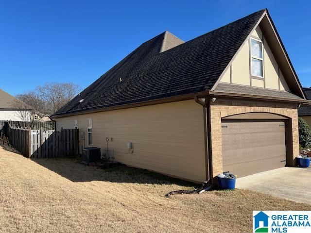 view of home's exterior with a garage, a shingled roof, fence, cooling unit, and brick siding