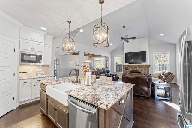 kitchen featuring dark wood finished floors, appliances with stainless steel finishes, a brick fireplace, vaulted ceiling, and a sink