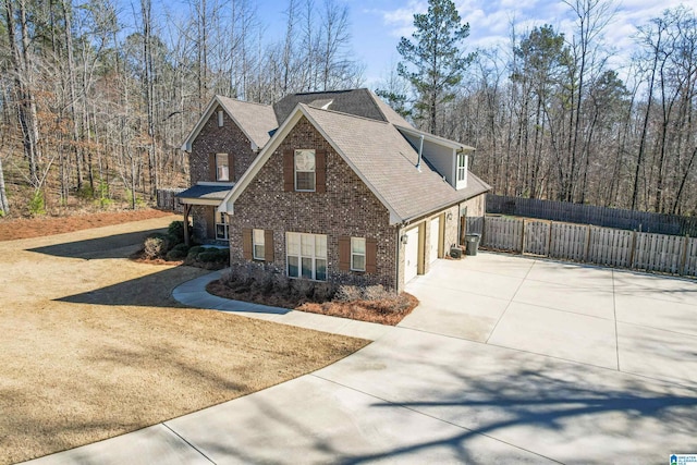 view of front facade with a shingled roof, fence, concrete driveway, and brick siding