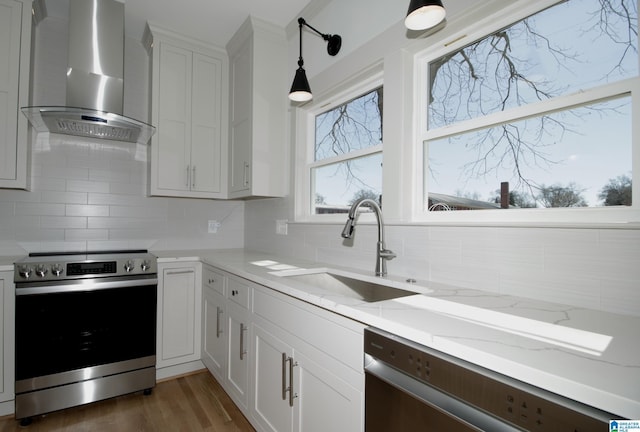 kitchen featuring stainless steel appliances, a sink, white cabinetry, wall chimney range hood, and backsplash