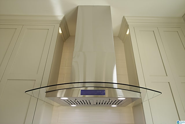 details featuring wall chimney exhaust hood and white cabinets