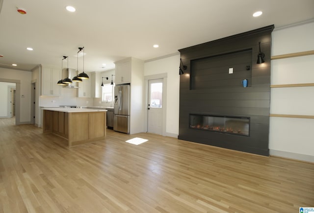 kitchen with light wood-style flooring, a fireplace, light countertops, wall chimney range hood, and stainless steel refrigerator with ice dispenser