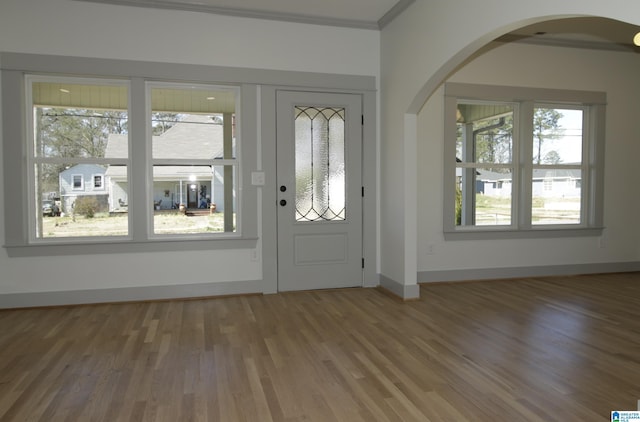 foyer featuring arched walkways, ornamental molding, wood finished floors, and baseboards