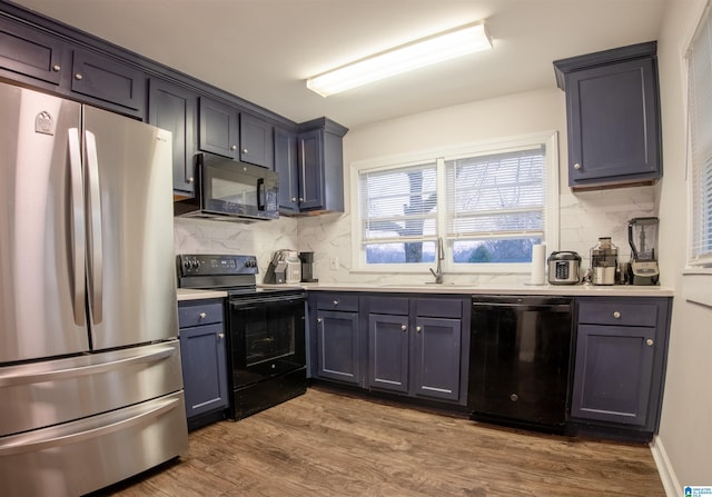 kitchen with black appliances, wood finished floors, light countertops, and a sink