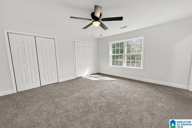 unfurnished bedroom featuring a ceiling fan, baseboards, visible vents, multiple closets, and carpet