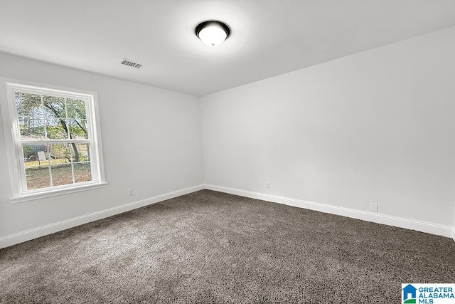 spare room with dark carpet, visible vents, and baseboards