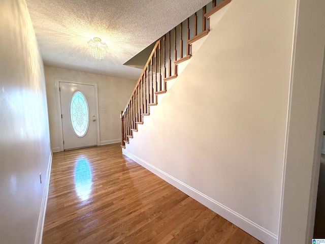 foyer entrance featuring a textured ceiling, stairway, wood finished floors, and baseboards