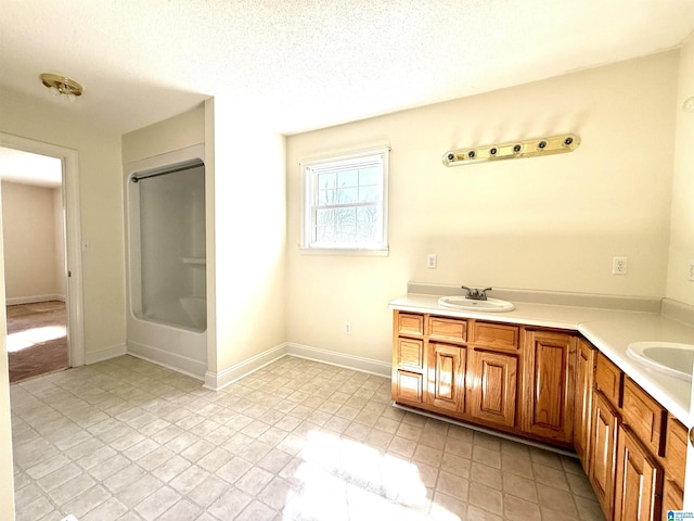 full bathroom featuring a textured ceiling, double vanity, a sink, and baseboards