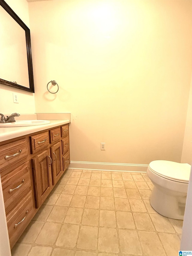 half bath with baseboards, vanity, and toilet