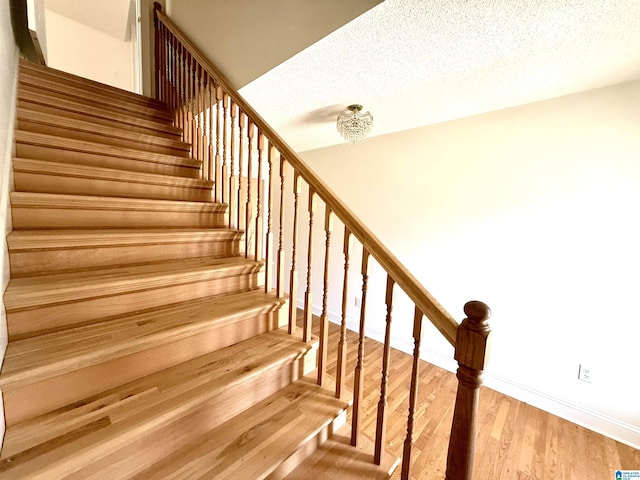 stairway featuring a textured ceiling, baseboards, and wood finished floors