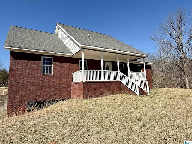 view of front of house featuring covered porch, brick siding, and roof with shingles