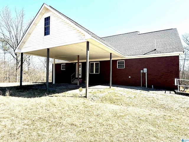 back of house with an attached carport, roof with shingles, and brick siding