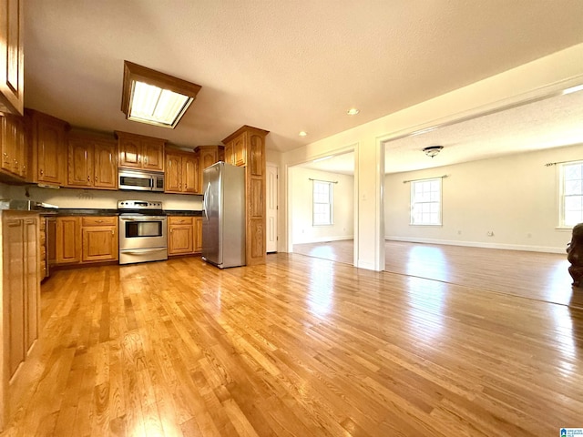 kitchen featuring dark countertops, brown cabinets, appliances with stainless steel finishes, and open floor plan