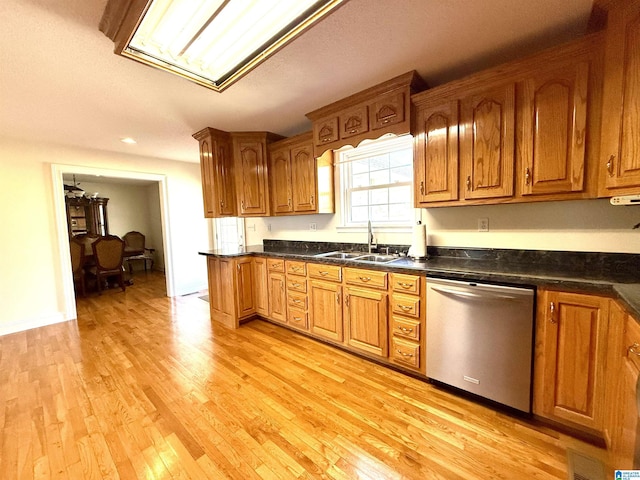 kitchen featuring dark countertops, light wood-style flooring, stainless steel dishwasher, brown cabinetry, and a sink