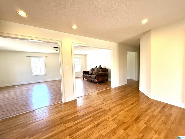 spare room with a textured ceiling, recessed lighting, wood finished floors, and baseboards