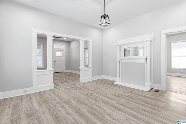 unfurnished dining area featuring baseboards, wood finished floors, visible vents, and ornate columns