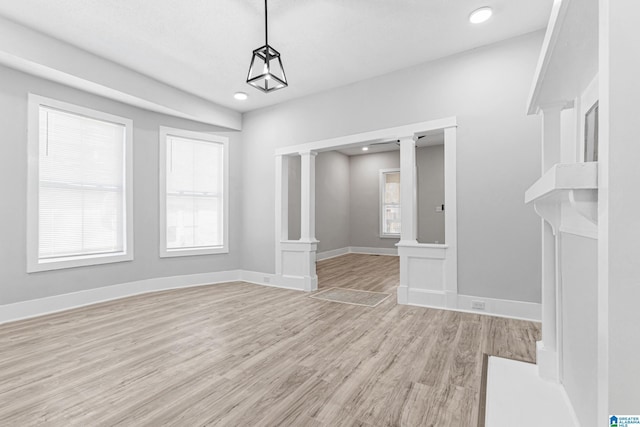 unfurnished dining area with decorative columns, baseboards, light wood-style flooring, and a wealth of natural light