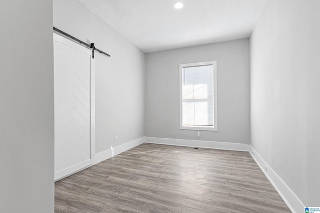 spare room featuring a barn door, a textured ceiling, baseboards, and wood finished floors