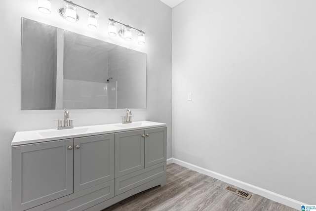 bathroom with wood finished floors, walk in shower, a sink, and visible vents