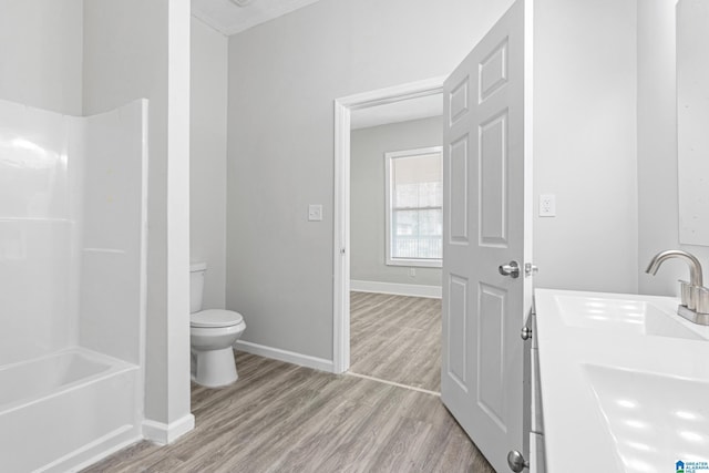 bathroom with baseboards, bathing tub / shower combination, toilet, wood finished floors, and a sink