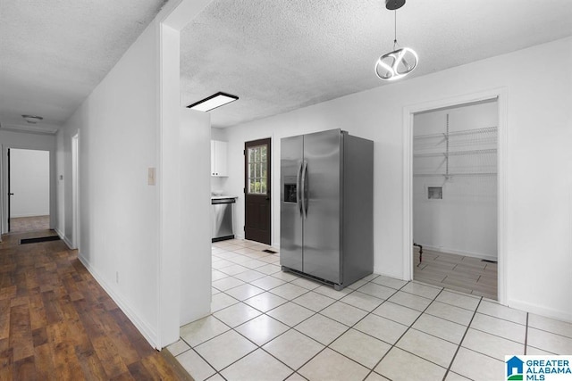 kitchen with a textured ceiling, light tile patterned floors, white cabinetry, appliances with stainless steel finishes, and pendant lighting