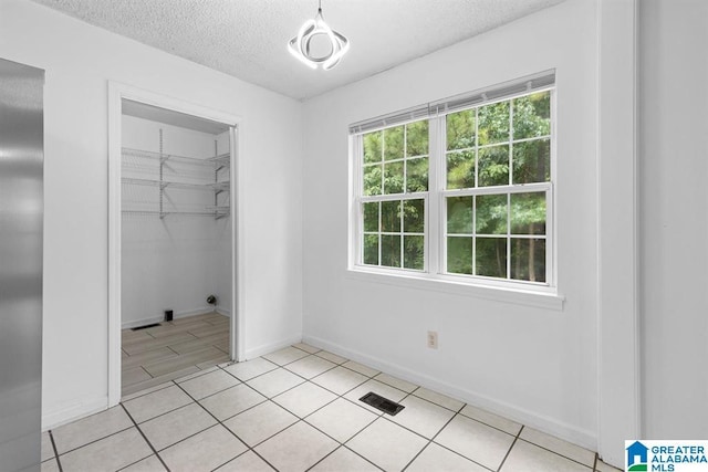 unfurnished bedroom featuring a textured ceiling, light tile patterned floors, visible vents, baseboards, and a closet