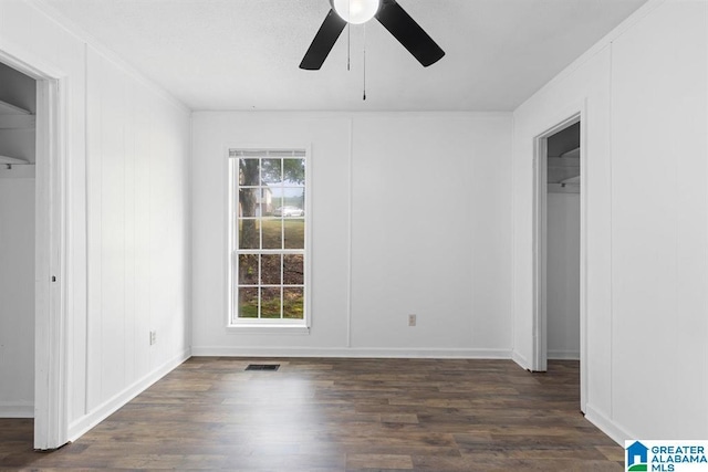 spare room featuring dark wood-type flooring, a decorative wall, visible vents, and a healthy amount of sunlight