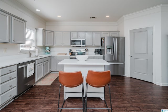 kitchen featuring gray cabinetry, appliances with stainless steel finishes, a sink, a kitchen island, and a kitchen breakfast bar