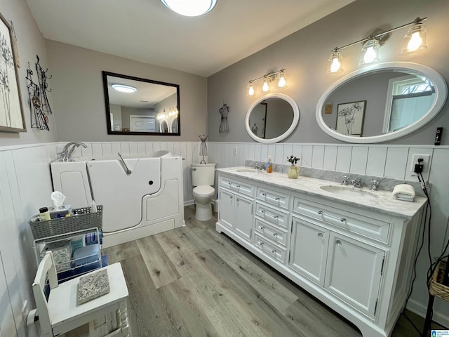 full bathroom with double vanity, a wainscoted wall, a sink, and wood finished floors