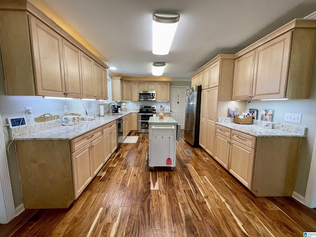 kitchen with light stone counters, dark wood-type flooring, a sink, appliances with stainless steel finishes, and light brown cabinetry