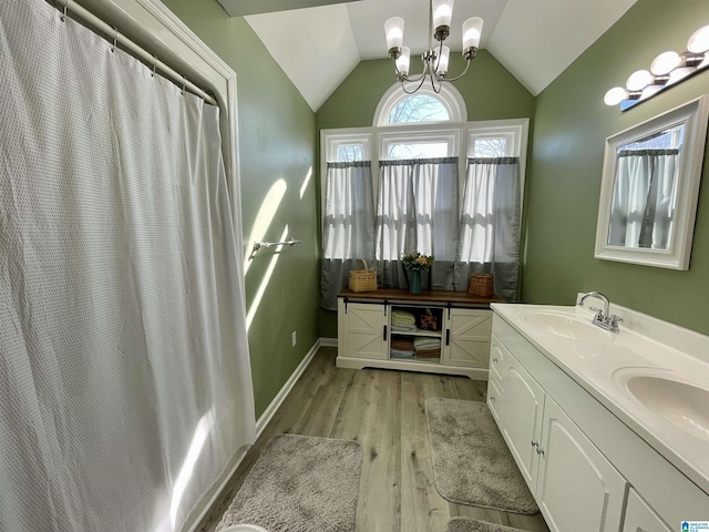 bathroom with a chandelier, wood finished floors, a sink, vaulted ceiling, and double vanity